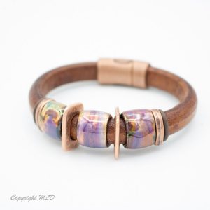 Tan bracelet with 3 purple and yellow beads with bronze flat spacers in between.